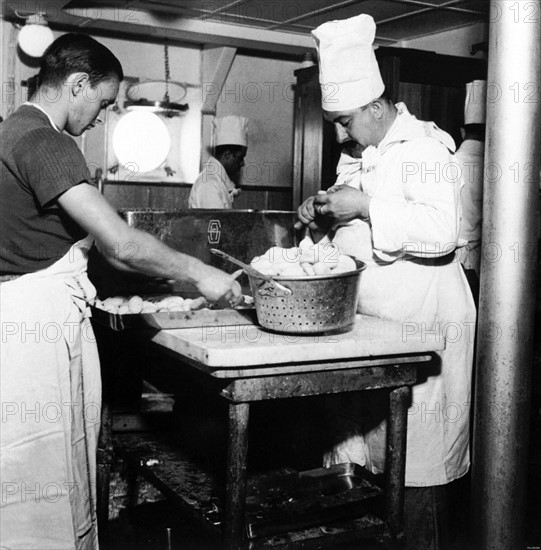 Le 19 août 1939, des cuisiniers s'affairent dans une partie  des cuisines du paquebot français PASTEUR.  Le paquebot PASTEUR, long de 212 mètres, d'une largeur de 27,52 mètres et pesant 35 000 tonneaux, accueille un grand nombre de passagers et de membres de l'équipage (officiers, personnels civils...). Au total, la population du paquebot s'élève à 1131 personnes.