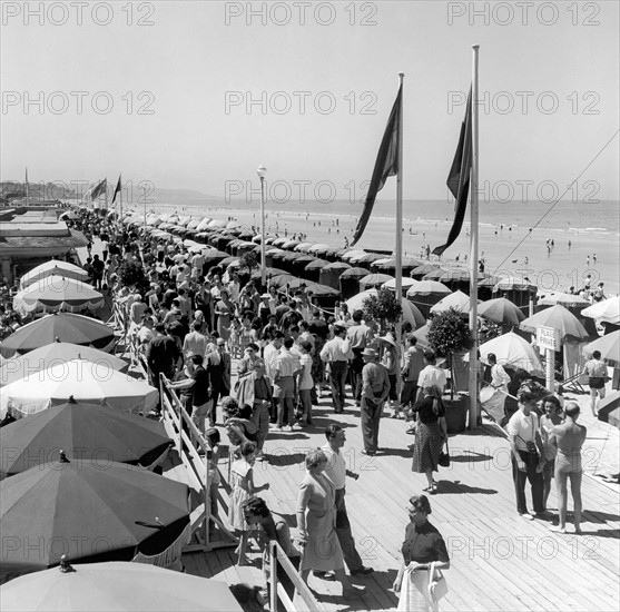 Juillet 1952, vacanciers se promenant sur les planches de Deauville (Calvados).