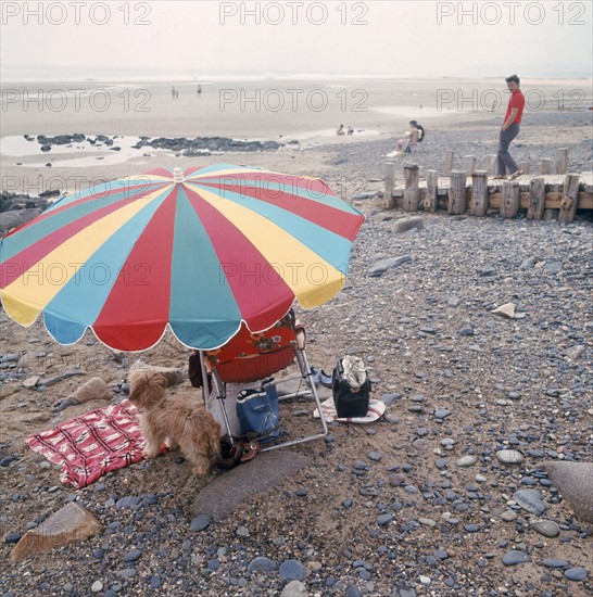 Dans les années 1970 sur une plage normande, vacanciers sous un parasol.