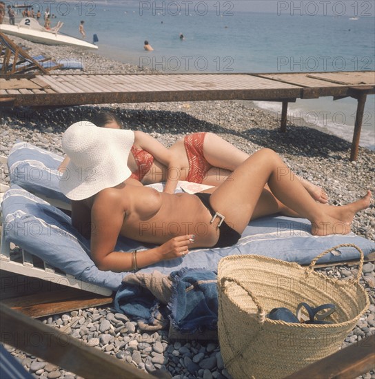 Dans les années 1970, deux femmes, dont l'une en monokini, bronzent sur une plage normande. Dans les annees 1970, deux femmes, dont l'une en monokini, bronzent sur une plage normande.