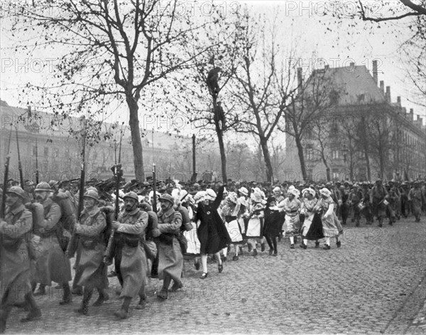 Défilé des troupes françaises à Metz auxquelles se mêlent des jeunes filles Lorraines enthousiastes après le 11 novembre 1918.