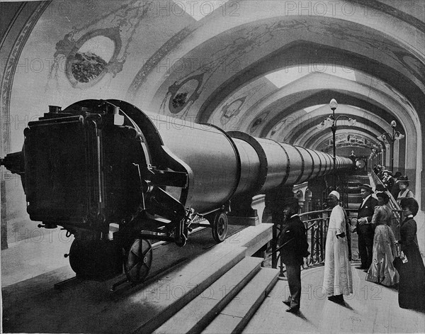 Exposition universelle de 1900 à Paris. La grande Lunette du Palais de l'Optique. Cette lunette colossale, le plus grande qui ait été construite jusqu'à ce jour, mesure 60 mètres de long sur 1 mètre 50 de diamètre, et pèse 20 000 kg. a l'une de ses extrémités, le Sidérostat de Foucault, animé d'un mouvement d'horlogerie, projette dans ce tube géant l'image de la lune.  Photographie parue dans "Le Panorama. L'Exposition universelle de 1900", publié sous la direction de René Baschet (Ludovic Baschet, éditeur).