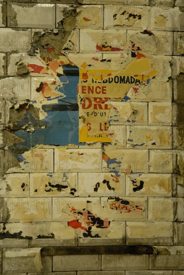 Affiche décollée sur un mur du métro parisien