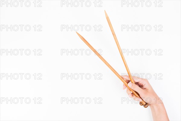 Woman hand with two wooden knitting needles over white background.