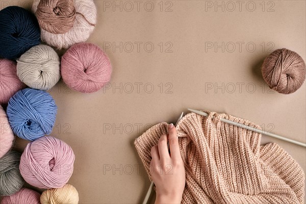 Close-up of female hands knitting wool sweater or plaid beige color. Top view