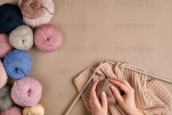 Close-up of female hands knitting wool sweater or plaid beige color. Top view