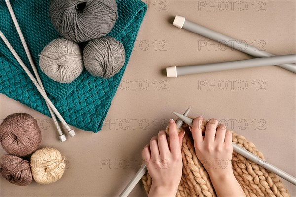 Close-up of female hands knitting wool sweater or plaid beige color. Top view