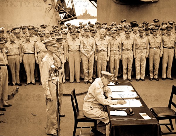 Gen. Douglas MacArthur signs as Supreme Allied Commander during formal surrender ceremonies on the USS MISSOURI in Tokyo Bay.  Behind Gen. MacArthur are Lt. Gen. Jonathan Wainwright and Lt. Gen. A. E. Percival.  September 2, 1945.  Lt. C. F. Wheeler. (Navy)