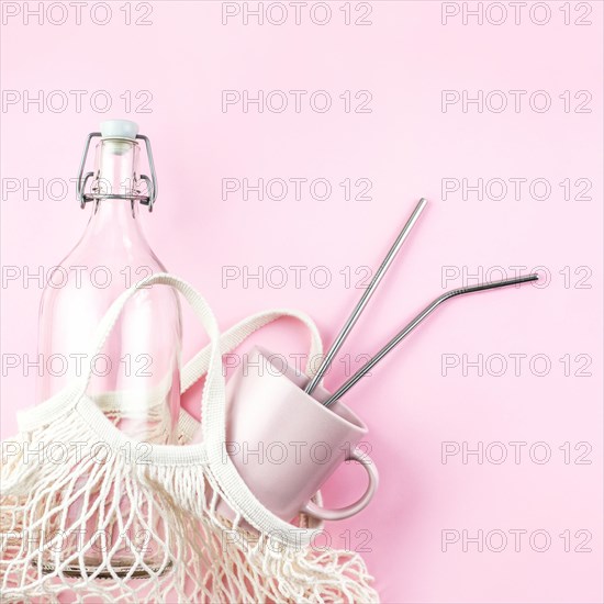 Mesh bag with reusable glass water bottle and cup on pink background. Sustainable lifestyle. Zero waste and no plastic concept.