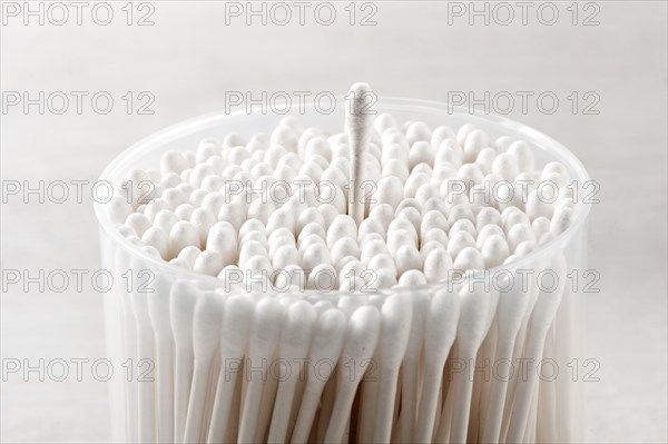Cotton buds in a plastic container with a single bud raised above the others over a gray background in a close up view