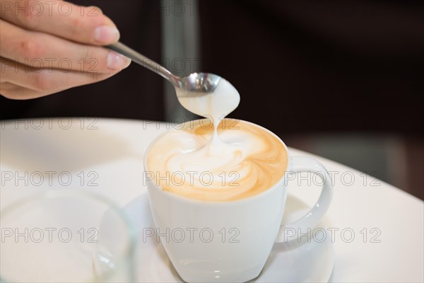 female hand holding a spoon over a hot cup of coffee Cappuccino