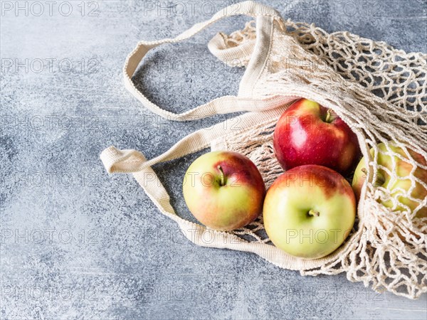 Eco-friendly beige shopping bag with red apples on a gray background. String bag with fruits. Zero waste, no plastic concept.
