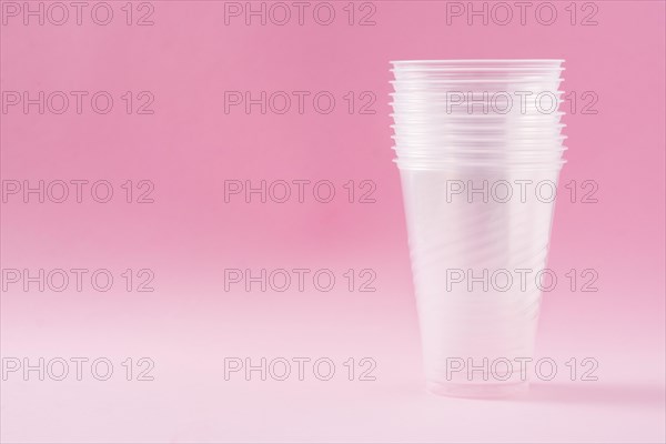 Disposable waste plastic glasses on pink background. Copyspace