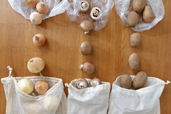 Thin plastic vs reusable cotton grocery bags with fresh produce on wooden background, zero waste concept.