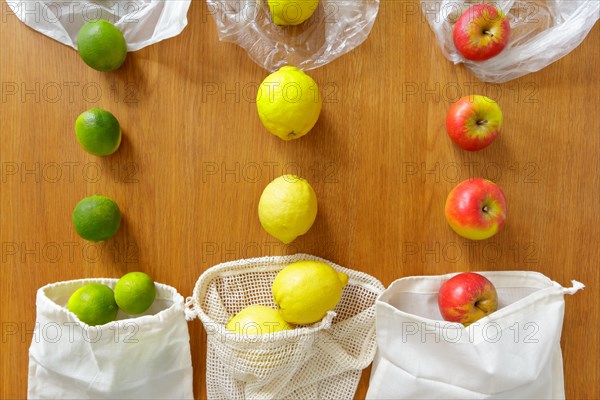 Thin poly versus cotton grocery bags with fresh fruits on wooden background, plastic free lifestyle concept.