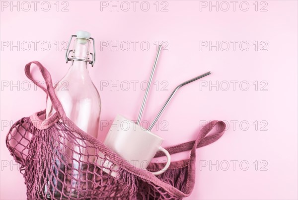 Mesh bag with reusable glass water bottle and cup on pink background. Sustainable lifestyle. Zero waste and no plastic concept.