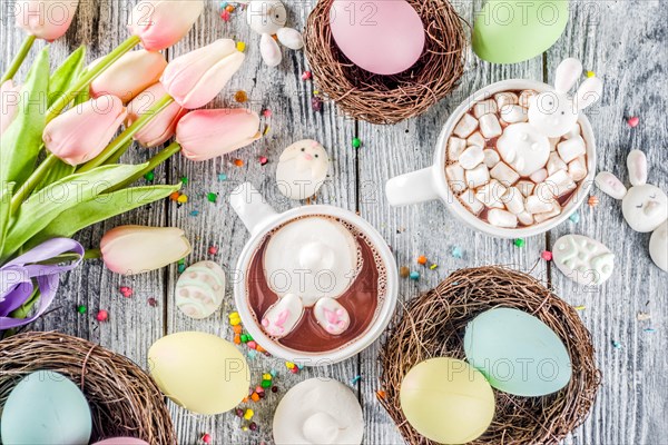 Easter funny kids food and drink concept, sweet hot chocolate with marshmallow bunny rabbits and easter eggs, wooden background copy space top view