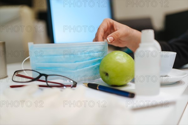 Glasses, face mask, gloves, hand sanitizer and apple on the office desk. COVID - 19 virus protection