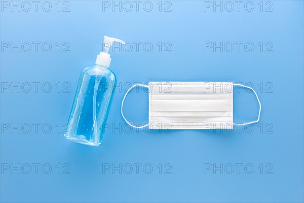 White medical mask and alcohol hand gel sanitizer to protect from virus and grem top view on blue background