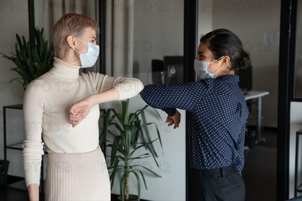 Female colleagues greeting in office touching elbows