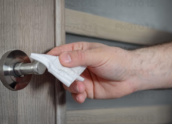 The hand of a man   who  disinfectes the doorknob  in the house with with antibacterial disinfecting wipe for killing corona virus on touching surface