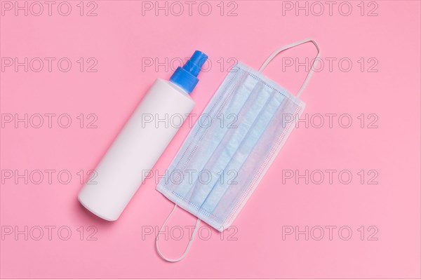 Coronavirus protection. Medical surgical mask and disinfectant or hand sanitizer on pink background. Hygiene measures to prevent spread of Covid-19 pa