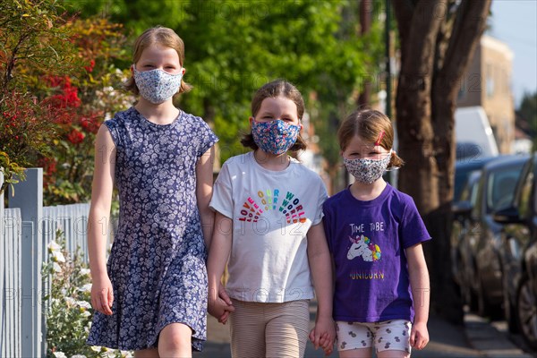 Three young sisters aged five years, 8 years & 10 years wearing masks that they've made at home with mum to wear during the COVID-19 / COVID 19 coronavirus pandemic of 2020; homemade face mask. UK. (118)