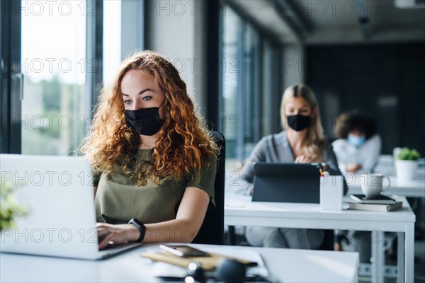 Young people with face masks back at work or school in office after lockdown.