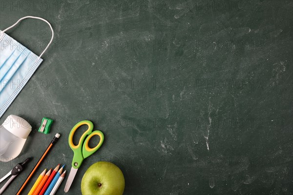 School educational supplies and covid-19 protection elements on green blackboard. Top view.