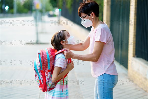 Mother preparing her little girl for the return to school wearing a mask.