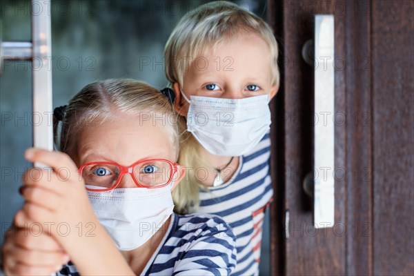 Little children looking unhappy and depressed after staying at home due banned street activity. Kids wearing medical face masks go out for  walk