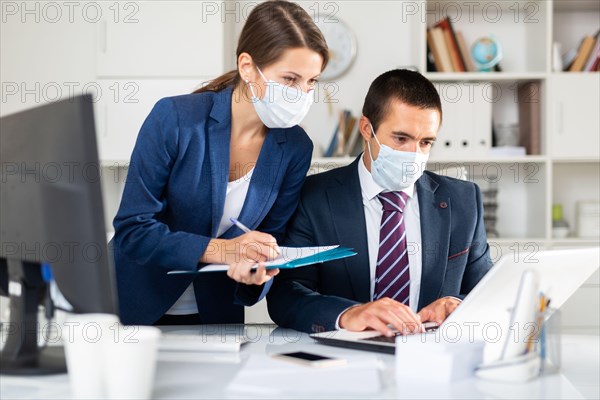 Portrait of two office employees in medical masks concentrating on work with papers and laptop. Necessary precautions during coronavirus pandemic