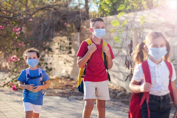 Pupils with medical masks on face and backpacks outdoor. Education during coronavirus time. Children and healthcare. Back to school.