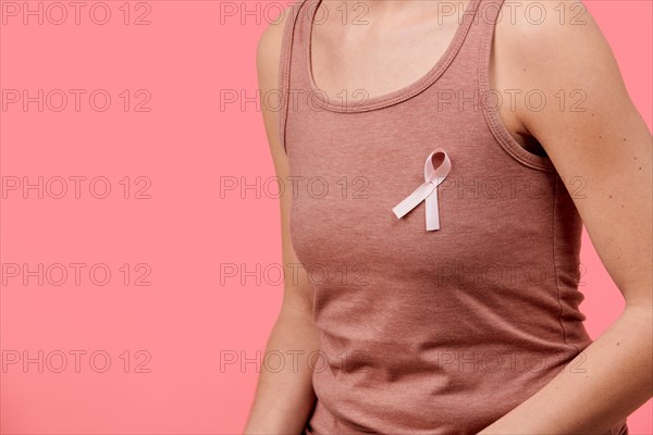 Midsection of a young woman wearing pink breast cancer awareness ribbon isolated over living coral background. Healthcare, people, charity and medicin