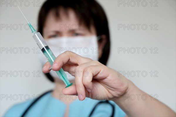 Doctor with syringe, woman in medical mask preparing to injection. Concept of vaccination, treatment of coronavirus infection