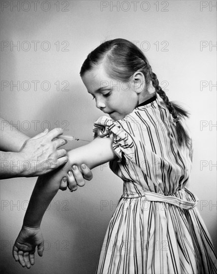 1950s YOUNG GIRL GETTING VACCINATION SHOT IN HER ARM