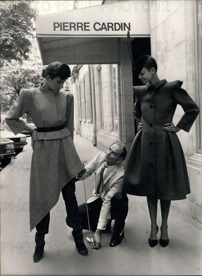 Jul. 22, 1979 - Pierre Cardin and his two models that are wearing pieces from his latest collection. On the left, she is wearing a suit jacket with a squared shoulder and an asymmetrical skirt over fitted pants. The jacket is beige and brick-red tartan and the pants are brick-red with maroon boots. On the right, she is wearing a frock coat made from green wool with black diamond-accented shoes and a black hat with a feather.