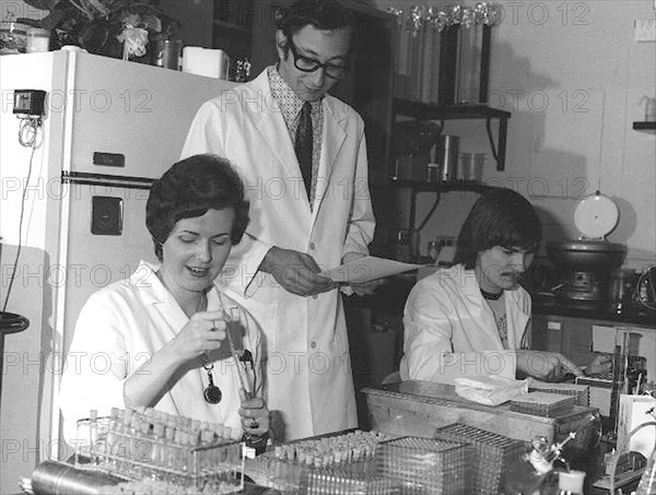 CDC Laboratorians. IMGSETINF, Lab technicians reading and checking serologies to determine presence of influenza A/NJ/8/76 (Swine Flu) and registering antibody rise to the swine influenza virus during vaccine testing trials. Standing at center is CDC virologist Dr. Alan Kendal. Image courtesy CDC/Katherine Lord, 1976.