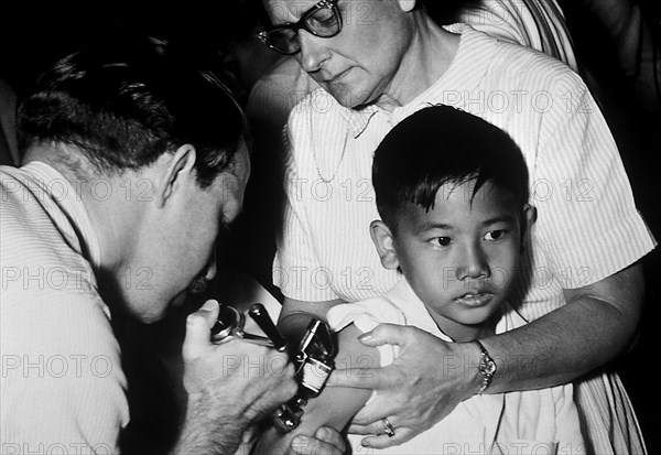 A jet injector gun being used during mass smallpox immunization procedures. Vaccinia vaccine is a highly effective immunizing agent that brought about the global eradication of smallpox, 1972. Because the smallpox vaccine is 'live', you can spread it to other people, as well as to other parts of one's own body. Image courtesy CDC/George Stenhouse.