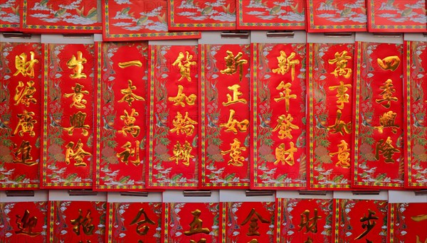 Chinese new year greetings printed with gold color on red paper hanging at a store, the chinese words mean wealth, prosperity and wishes come true