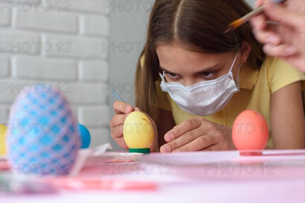 Close-up of a girl in a medical mask who paints Easter eggs