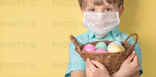 Covid easter concept - boy holds basket with easter eggs wearing medical mask