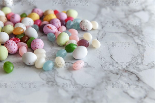 Happy Easter concept. Preparation for holiday. Easter candy chocolate eggs and jellybean sweets on trendy gray marble background. Simple minimalism fl
