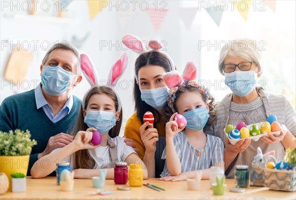 Mother, grandparents and children are painting eggs. Happy family are preparing for Easter. Cute little girls wearing bunny ears.