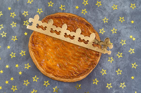 Galette des rois, french kingcake with a golden crown on a grey slate background scattered with golden stars