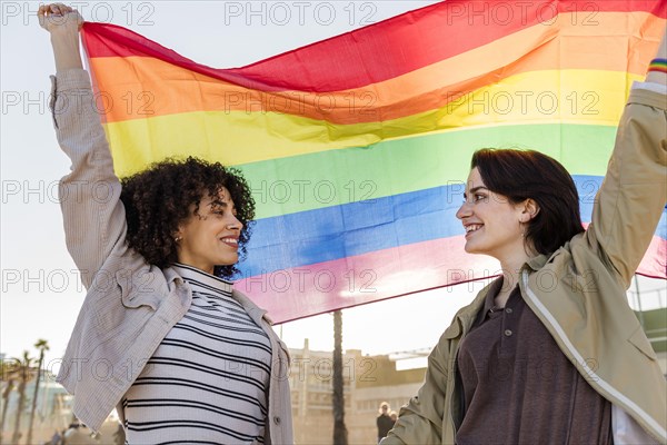interracial lesbian couple of smiling girls waving the rainbow flag, symbol of the struggle for gay rights, concept of sexual freedom and racial diver