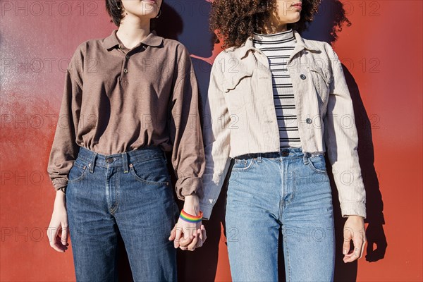 interracial lesbian couple of young women holding hands in front of a red wall, concept of sexual freedom and racial diversity