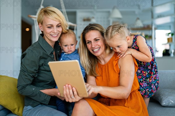 Happy lesbian couple playing, spending time with children at home