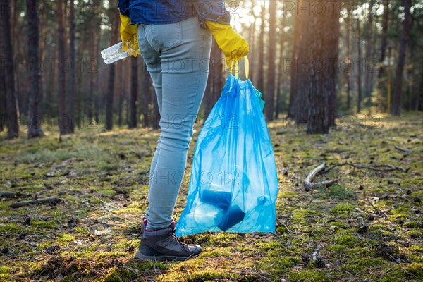 Keep our planet clean! Volunteer holding plastic bag and cleaning forest from plastic pollution. Environmental conversation