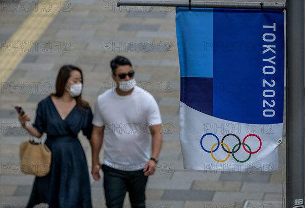 Tokyo, Japan. 09 May, 2021. A couple walks by a Tokyo 2020 flag ahead of the protest against the Tokyo Olympics in front of the New National Stadium, the main stadium for the Tokyo Olympics. Credit: ASWphoto/Alamy Live News